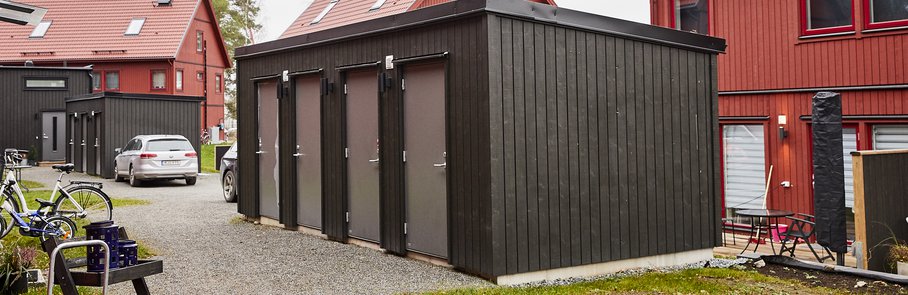 Svart separat träbyggnad med fyra förråd som hör till nybyggda parhus i Väsjön.