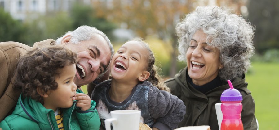 Playful grandparents and grandchildren laughing, eating lunch in park