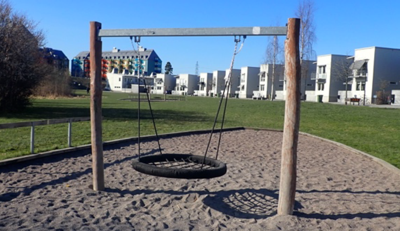 En lekplats med en gungställning och en byggnad i bakgrunden.