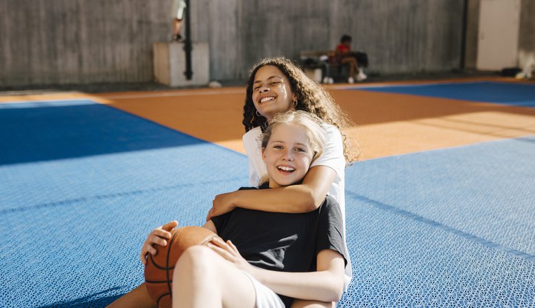 Smiling female friends sitting in basketball court