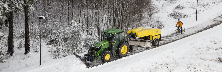 Vintercykling, en traktor med snöplog och påkopplad sopmaskin. En cykel som följer ekipaget.